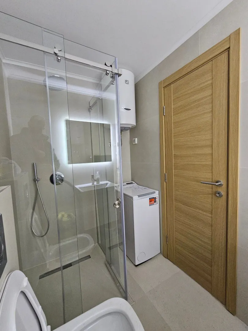 Modern bathroom with a walk-in shower, washbasin, and washing machine.
