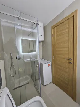 Modern bathroom with a walk-in shower, washbasin, and washing machine. - image 9
