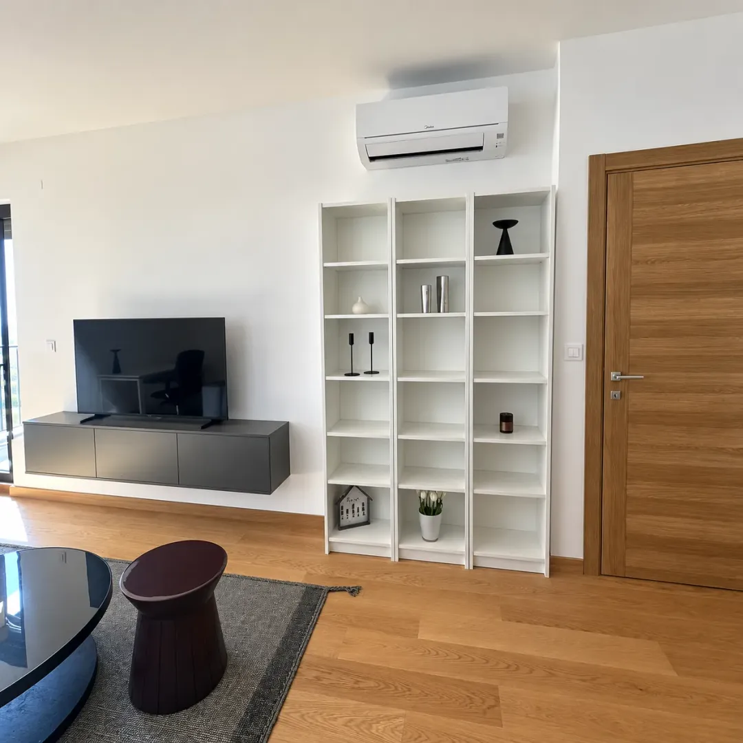 Living room with a TV, white bookshelves, and an air conditioning unit on the wall.