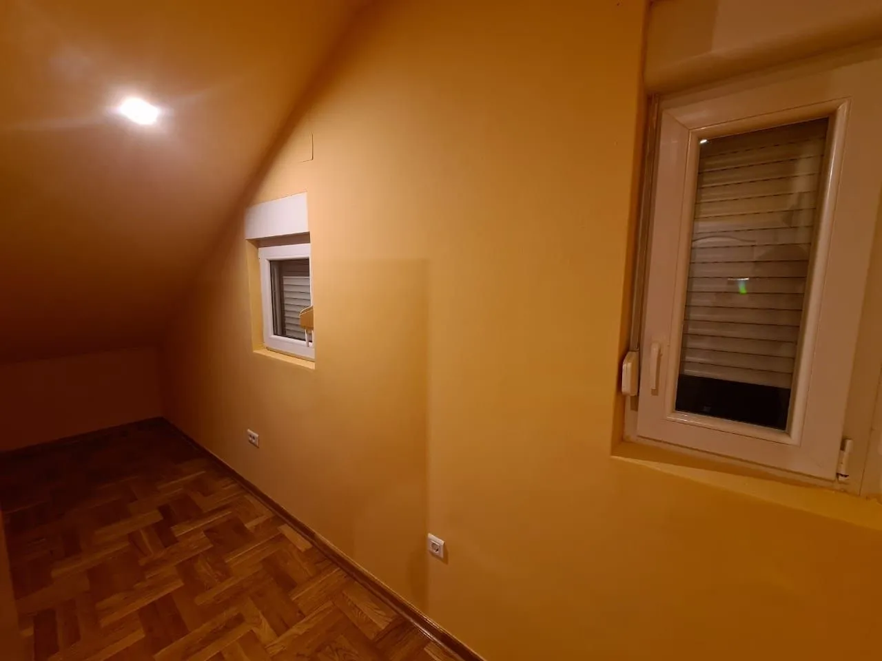 Prazna soba u potkrovlju sa parketom i žutim zidovima.