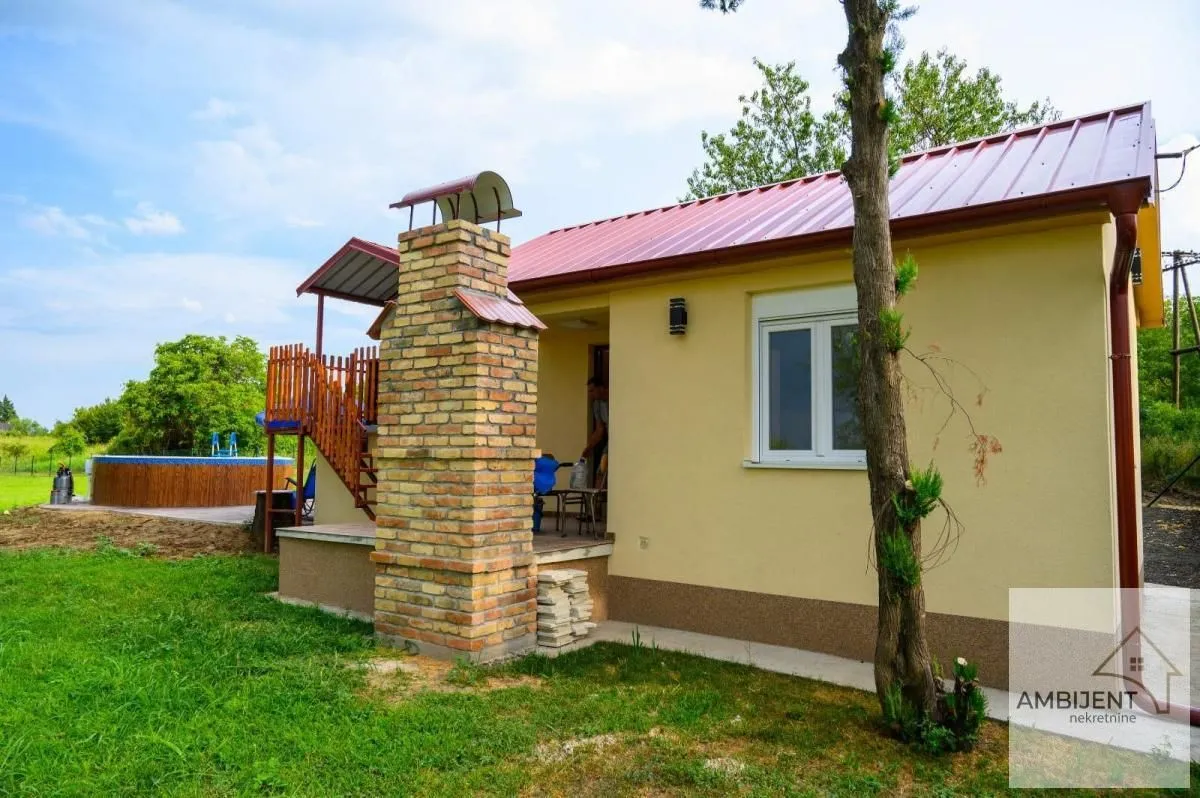 Pogled na spoljašnjost prizemne kuće sa dimnjakom, dvorištem i bazenom.