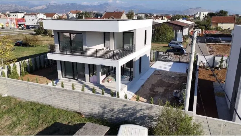 Pogled iz vazduha na modernu dvospratnu kuću sa dvorištem i ogradom.