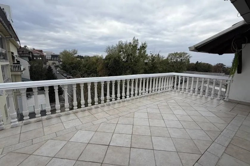 Velika popločana terasa sa belom ogradom i pogledom na okolinu.
