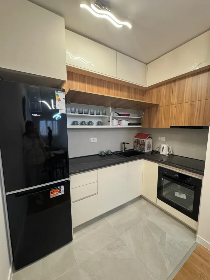 Modern kitchen with white and wooden cabinets and a black refrigerator.