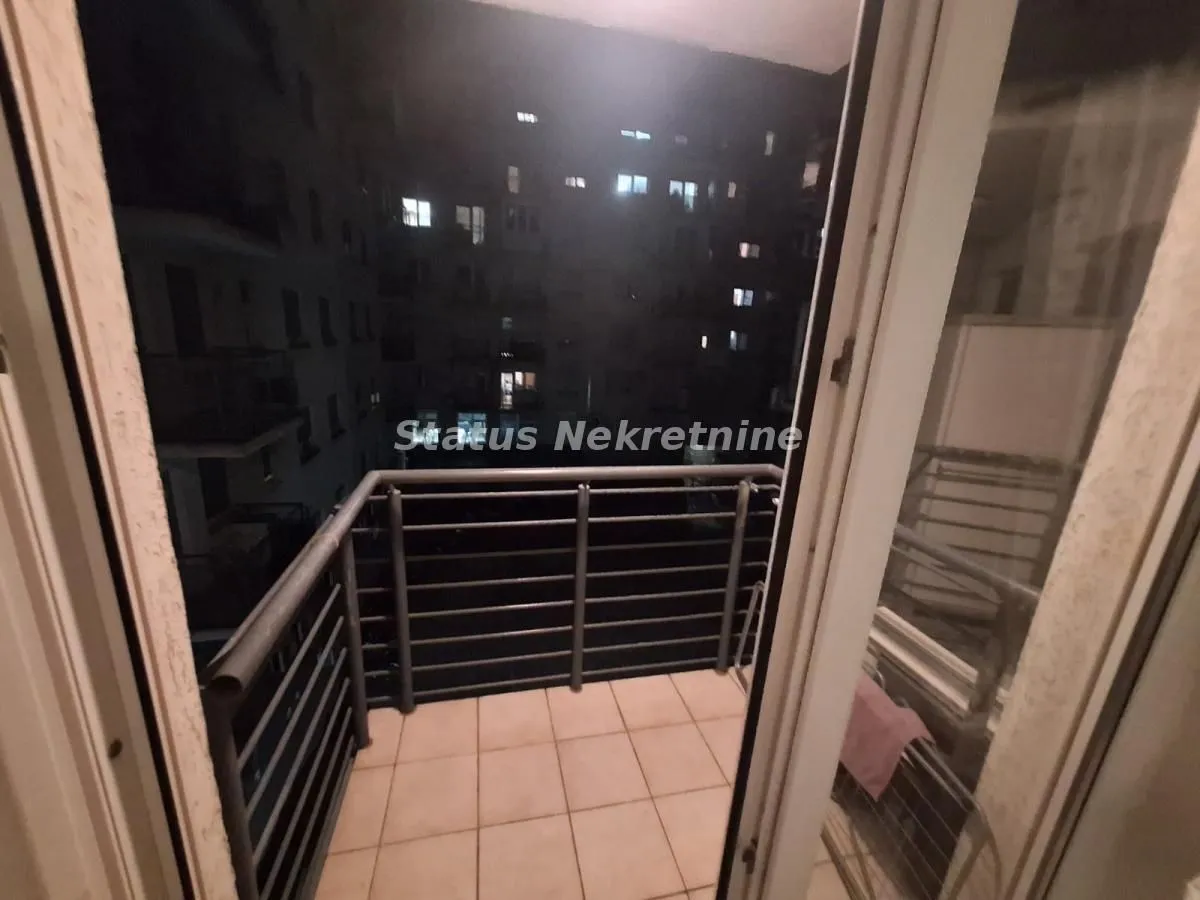Manji popločani balkon sa metalnom ogradom i pogledom noću na okolne zgrade.