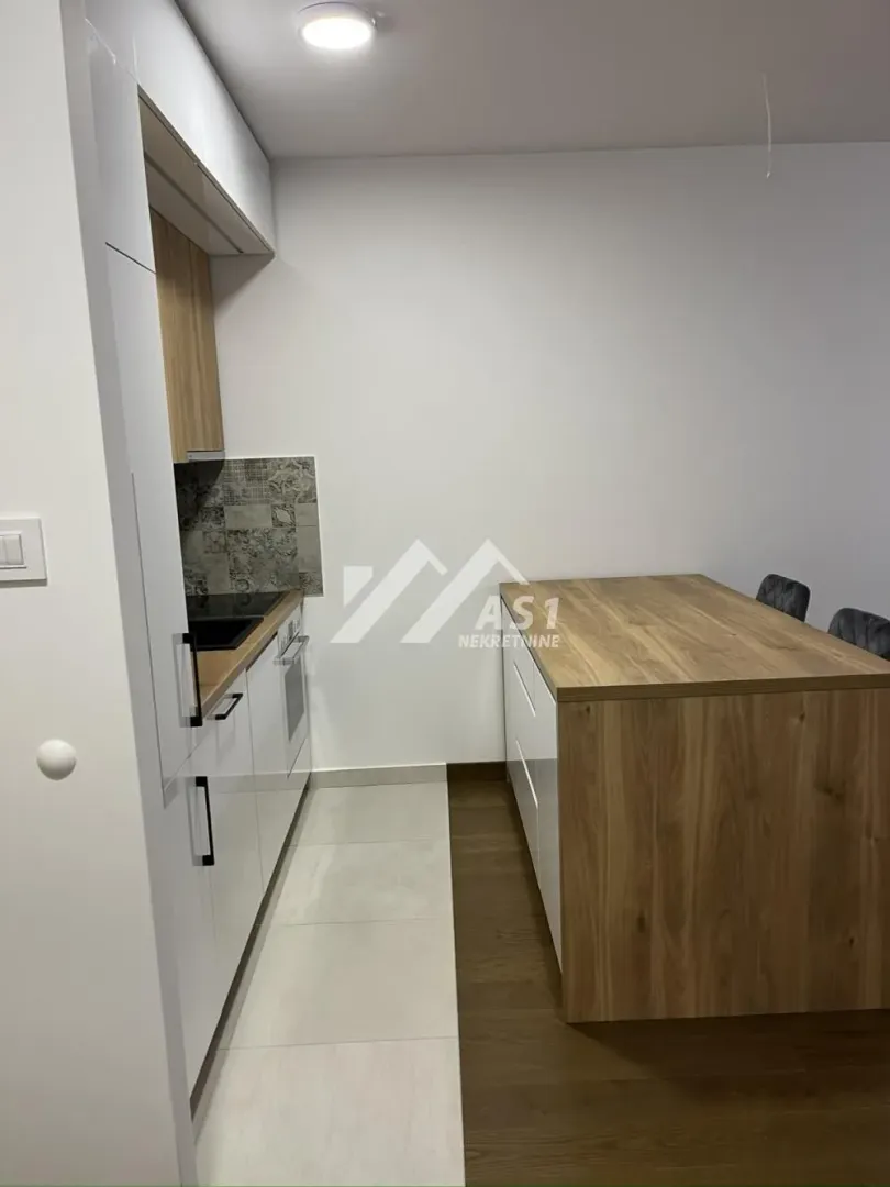 Moderna kuhinja sa belim elementima i trpezarijskim stolom.