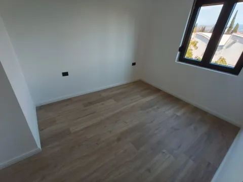 Prazna soba sa bijelim zidovima, drvenim podom i prozorom. - image 3
