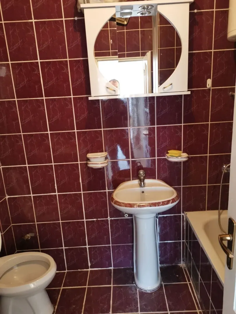 Kupatilo sa tamnocrvenim pločicama, lavaboom i ogledalom sa ormarićem.
