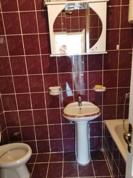 Kupatilo sa tamnocrvenim pločicama, lavaboom i ogledalom sa ormarićem. - image 4