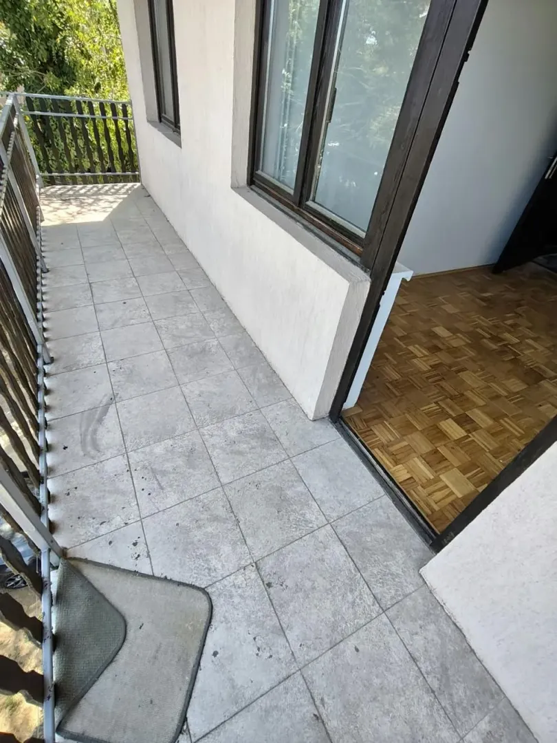 Nenamešten balkon sa popločanim podom i izlazom u sobu.