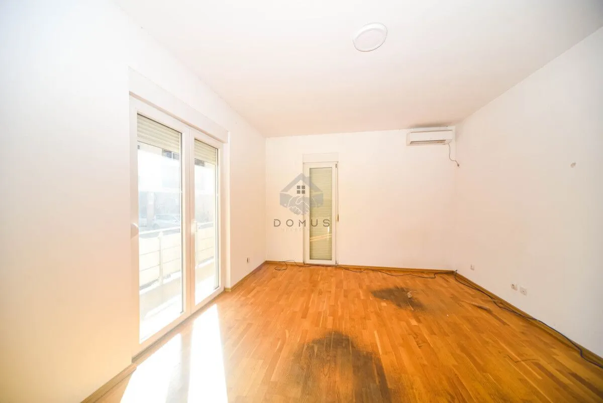Empty room with wooden flooring, white walls and balcony doors.