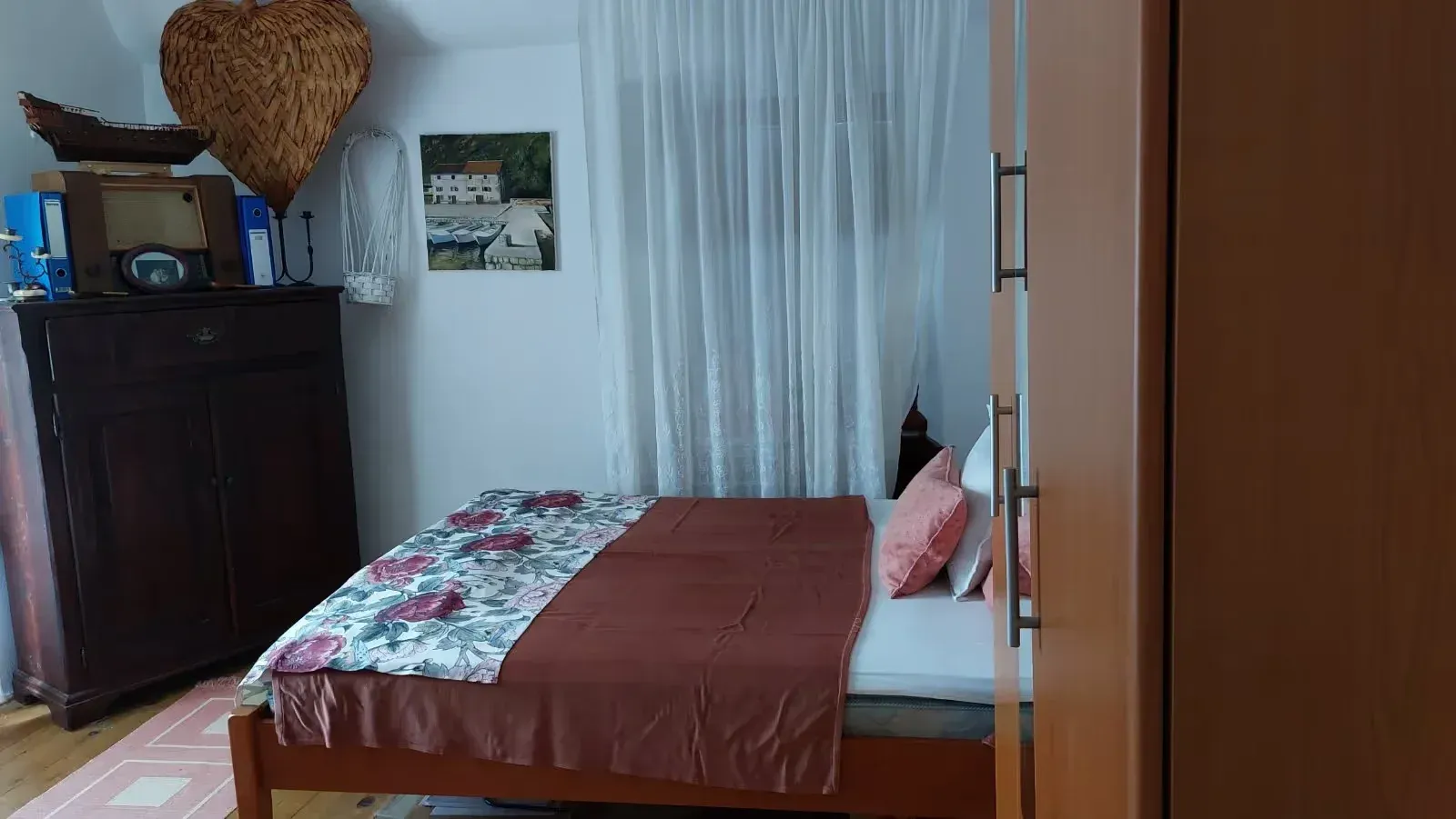 Spavaća soba sa bračnim krevetom, drvenim ormarom i komodom.