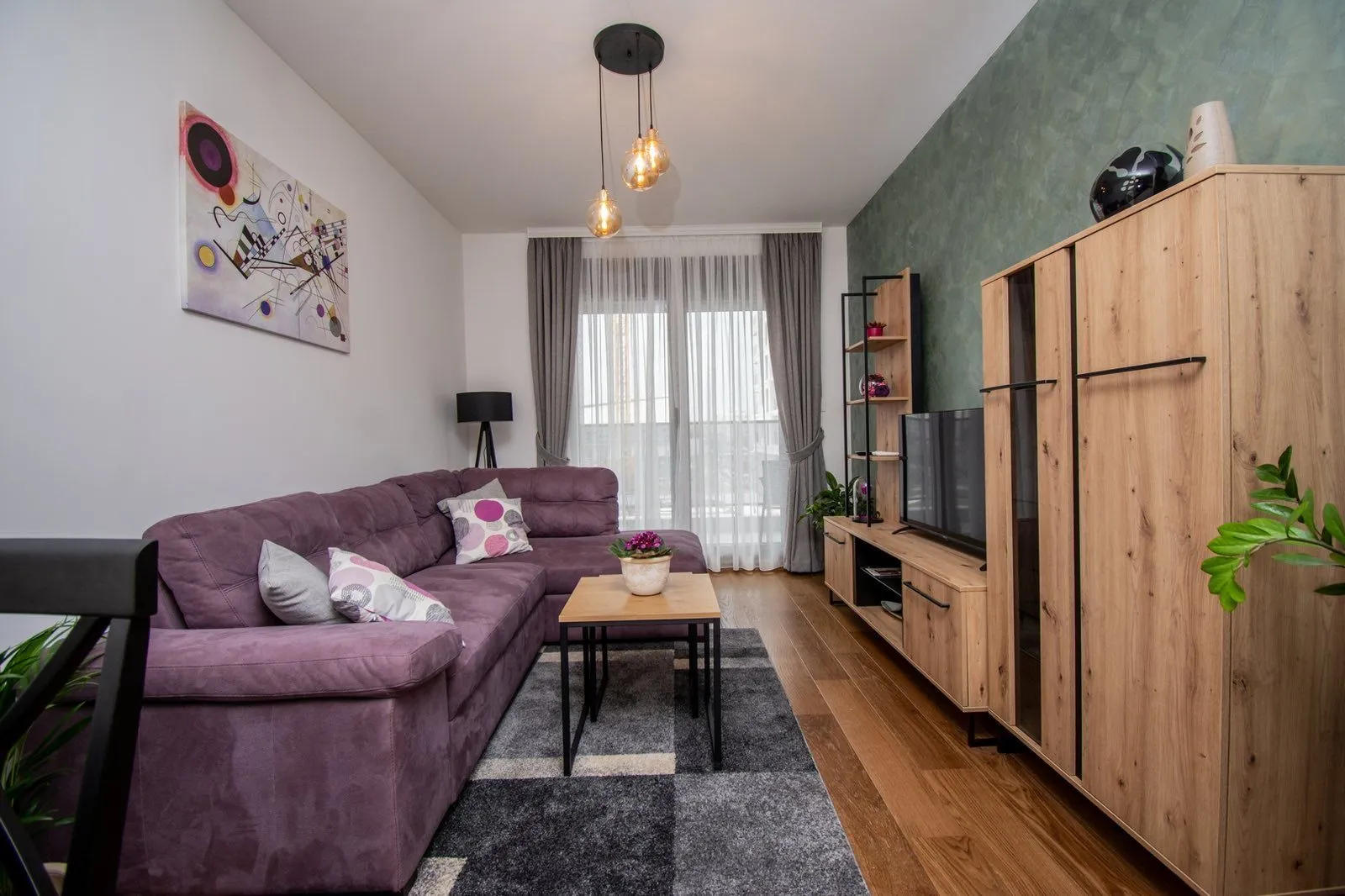 Moderna i uredna dnevna soba sa ljubičastom ugaonom garniturom.