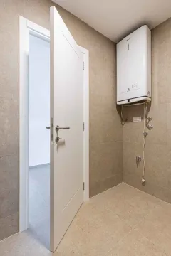 Kupatilo sa pločicama u neutralnim tonovima, bojlerom na zidu i otvorenim vratima. - image 21