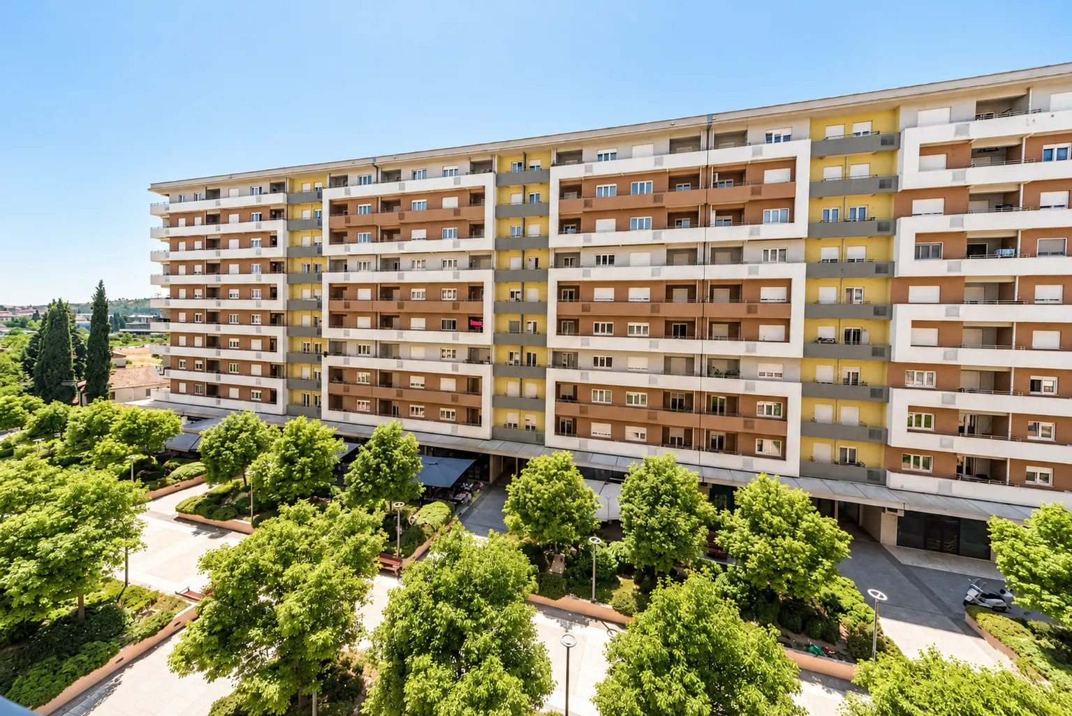 View from the terrace facing a multi-story residential building and landscaped courtyard greenery.