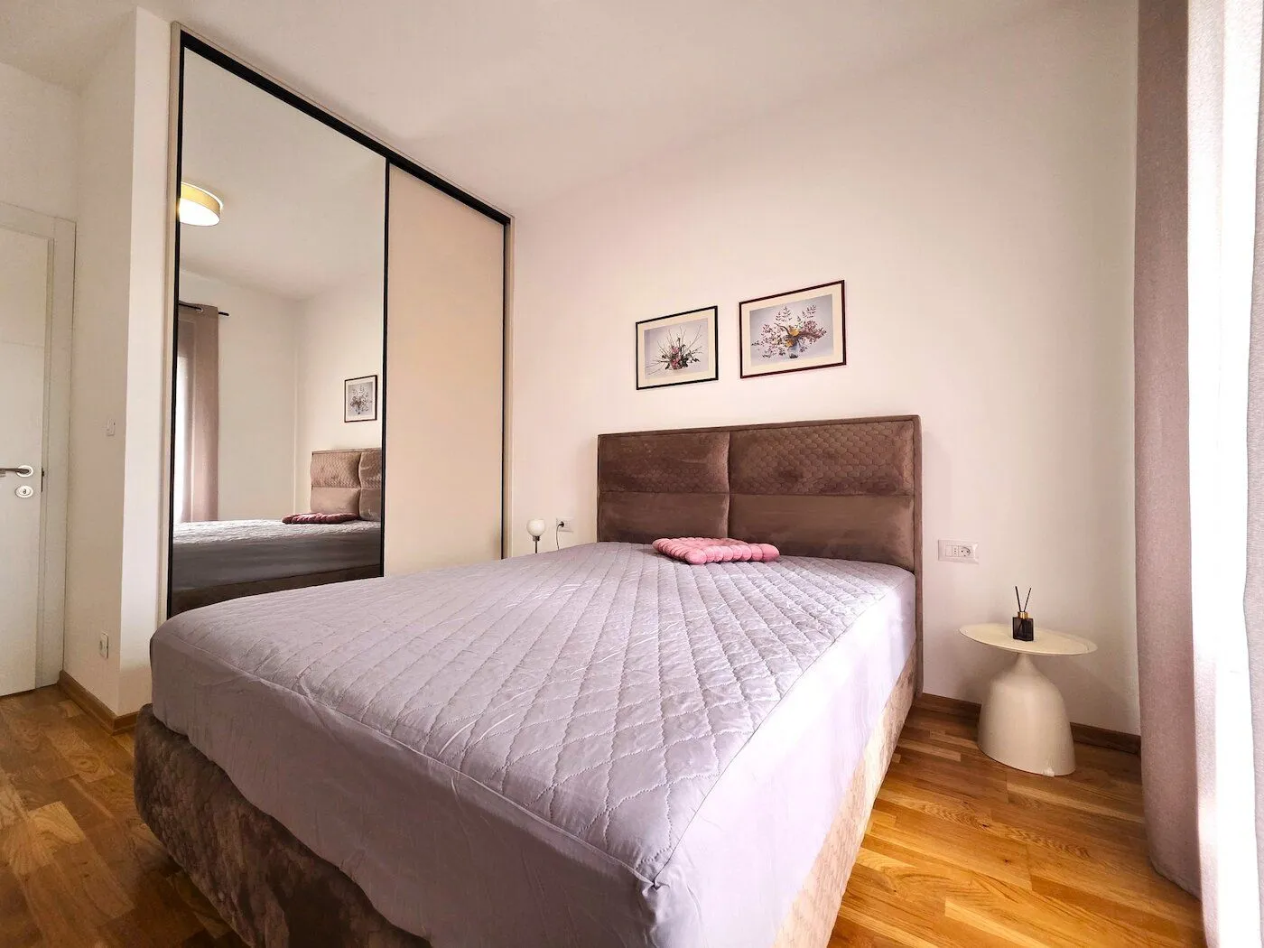 Furnished bedroom with a double bed, mirrored wardrobe, and hardwood flooring.
