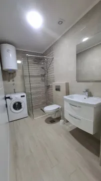 Modernly equipped bathroom with a walk-in shower, washbasin, and washing machine. - image 5