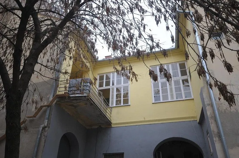 Pogled na dvorišnu fasadu zgrade sa balkonima i drvećem u prvom planu.
