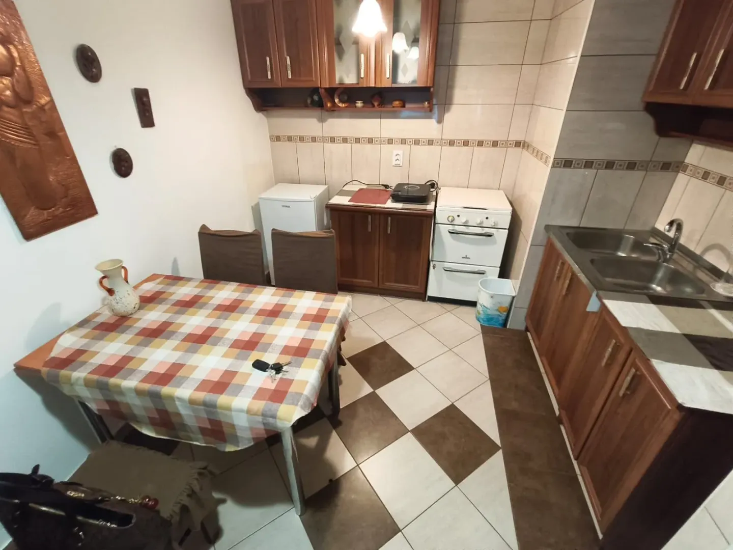 Kuhinja sa drvenim elementima i trpezarijskim stolom sa kariranim stolnjakom.