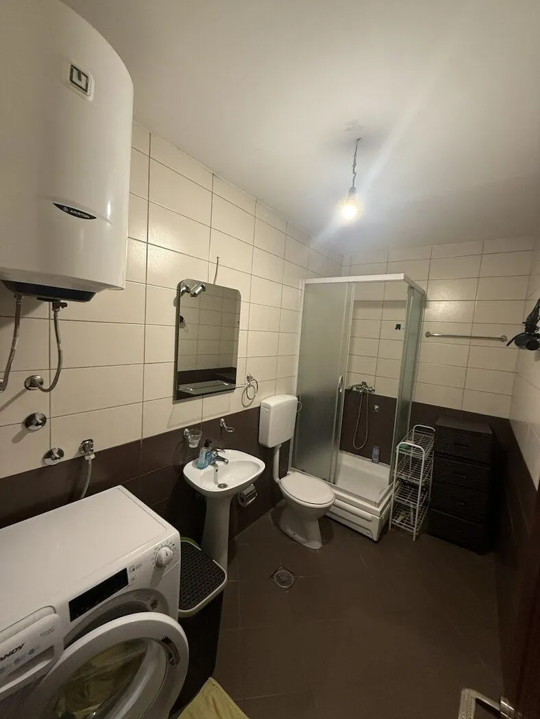 Smaller bathroom with a shower cabin, sink, toilet, and washing machine.