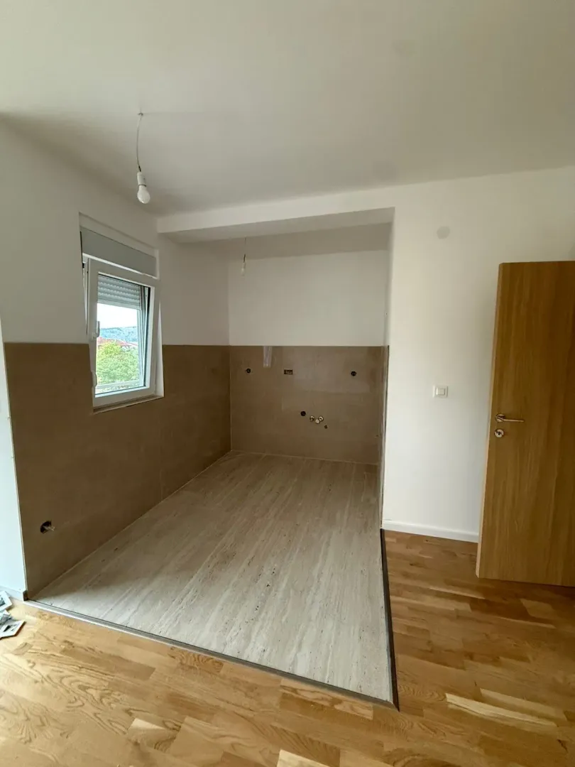 Pogled na nenamješten prostor sa pripremljenim priključcima za kuhinju i prozorom.