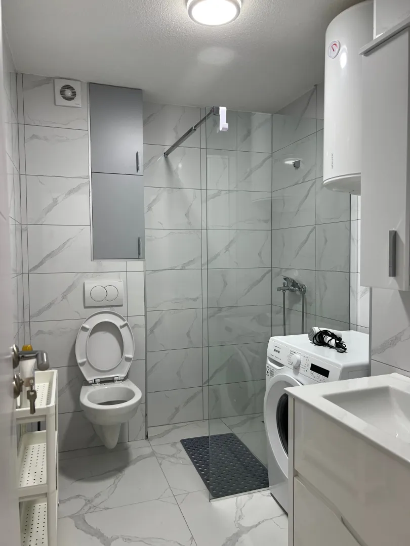 Moderno opremljeno kupatilo sa tuš kabinom i veš mašinom.