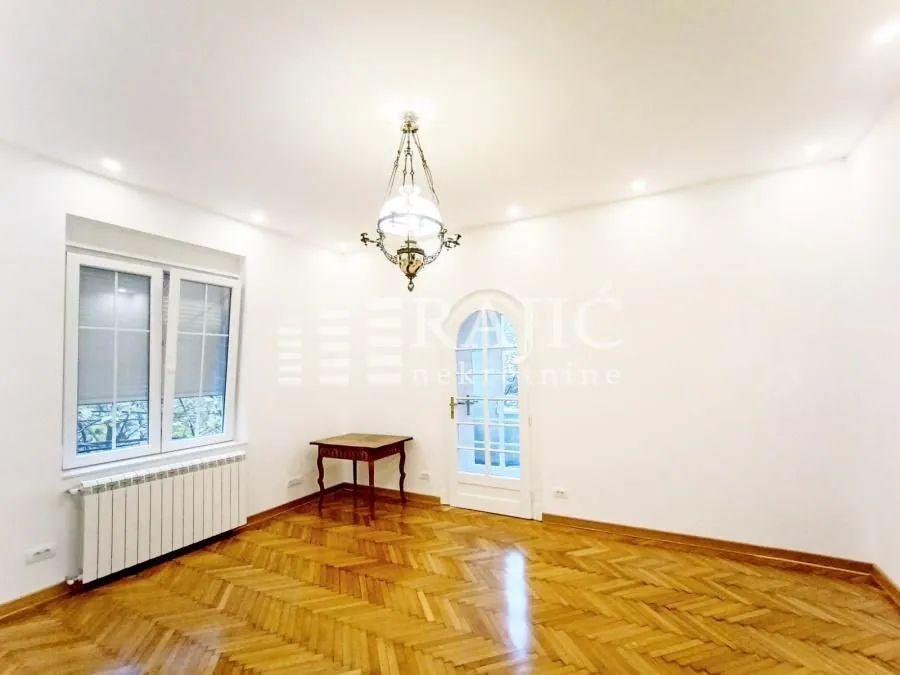 Bright empty room with parquet flooring and a chandelier.
