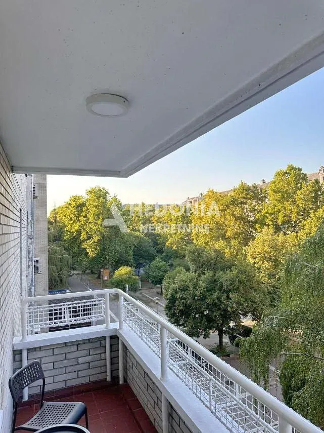 Natkriven balkon sa pogledom na zelenilo i okolne zgrade.
