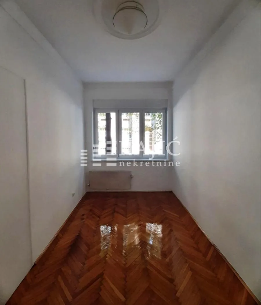 Empty room with wooden parquet flooring and a window.