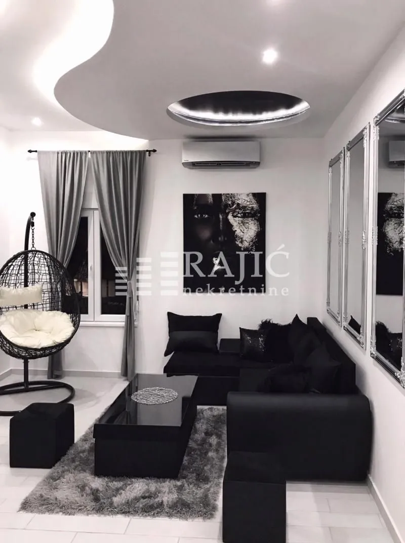 Modern living room with a black sectional sofa and decorative ceiling lighting.