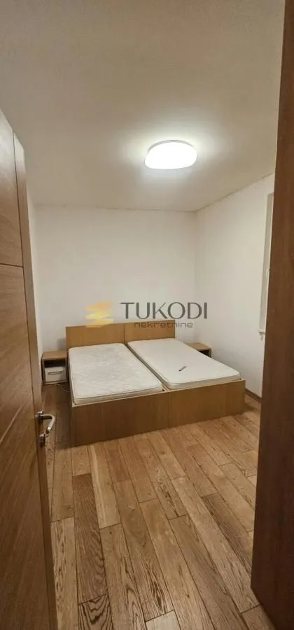 Spavaća soba sa dva spojena kreveta i drvenim podom.