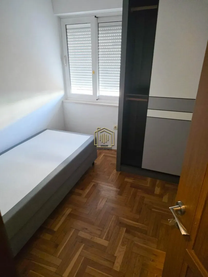 Manja spavaća soba sa krevetom, ormarom i parketom.