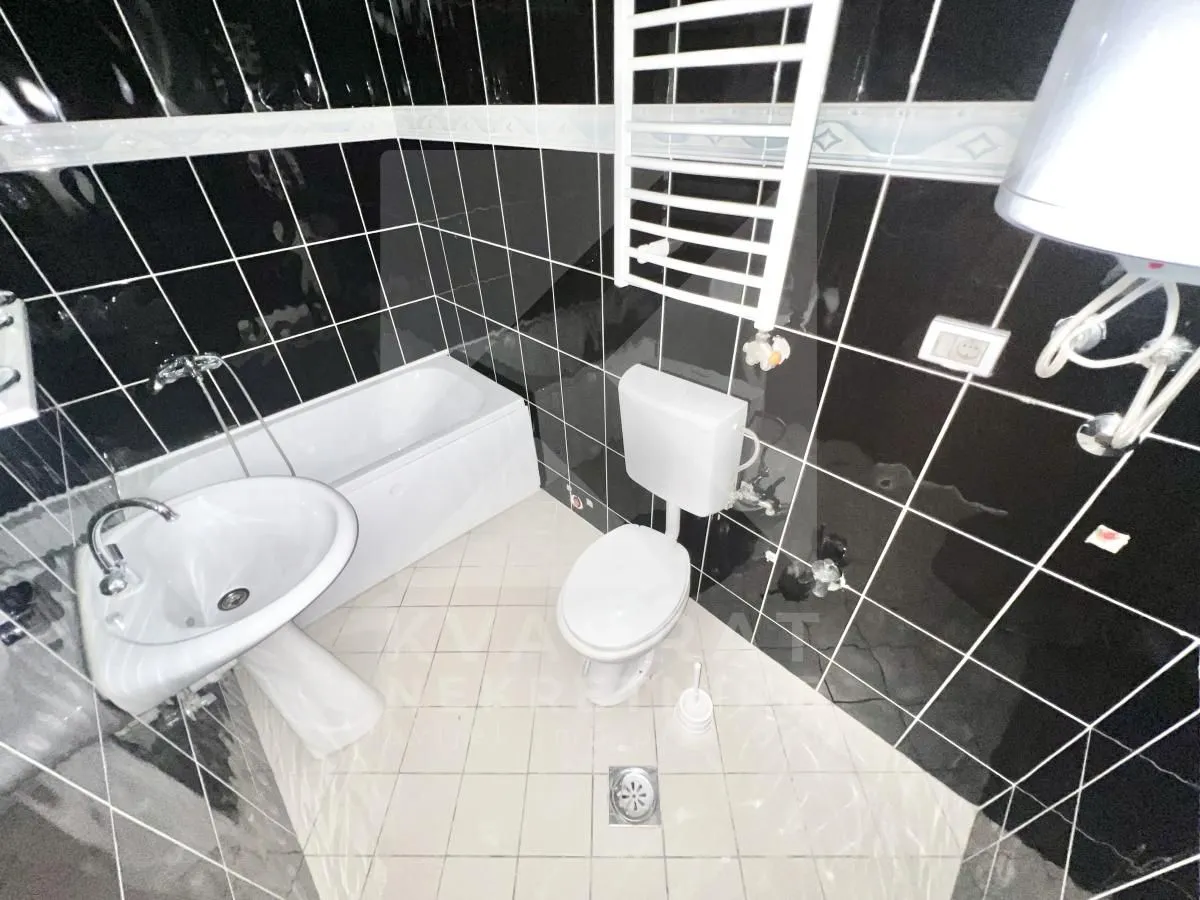 Bathroom equipped with a bathtub, washbasin, and toilet, tiled in black.
