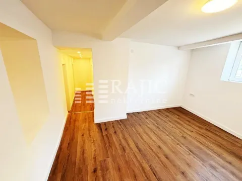 Empty room with laminate flooring and white walls, with a hallway in the background. - image 12