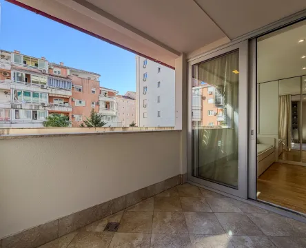 Natkriveni balkon sa pogledom na okolne zgrade i izlazom u enterijer kroz klizna vrata. - image 13