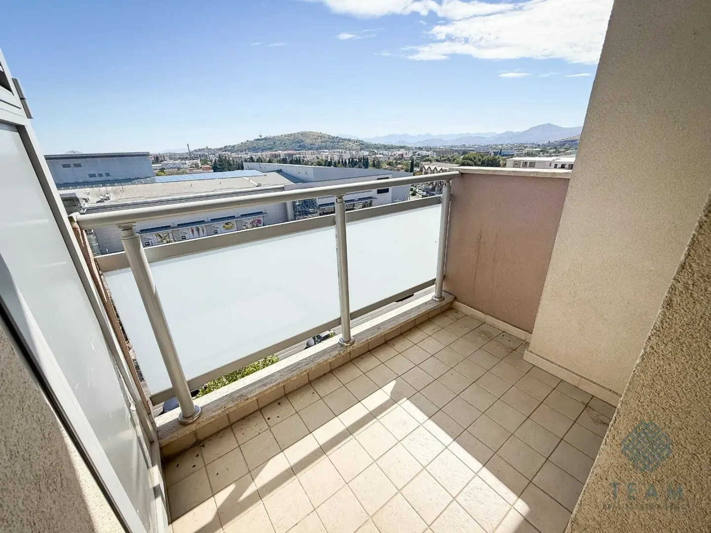 Small tiled balcony with glass railing and city view.