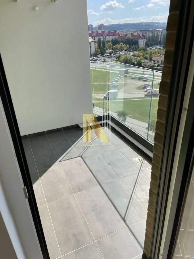 Manji popločani balkon sa staklenom ogradom i pogledom na naselje.