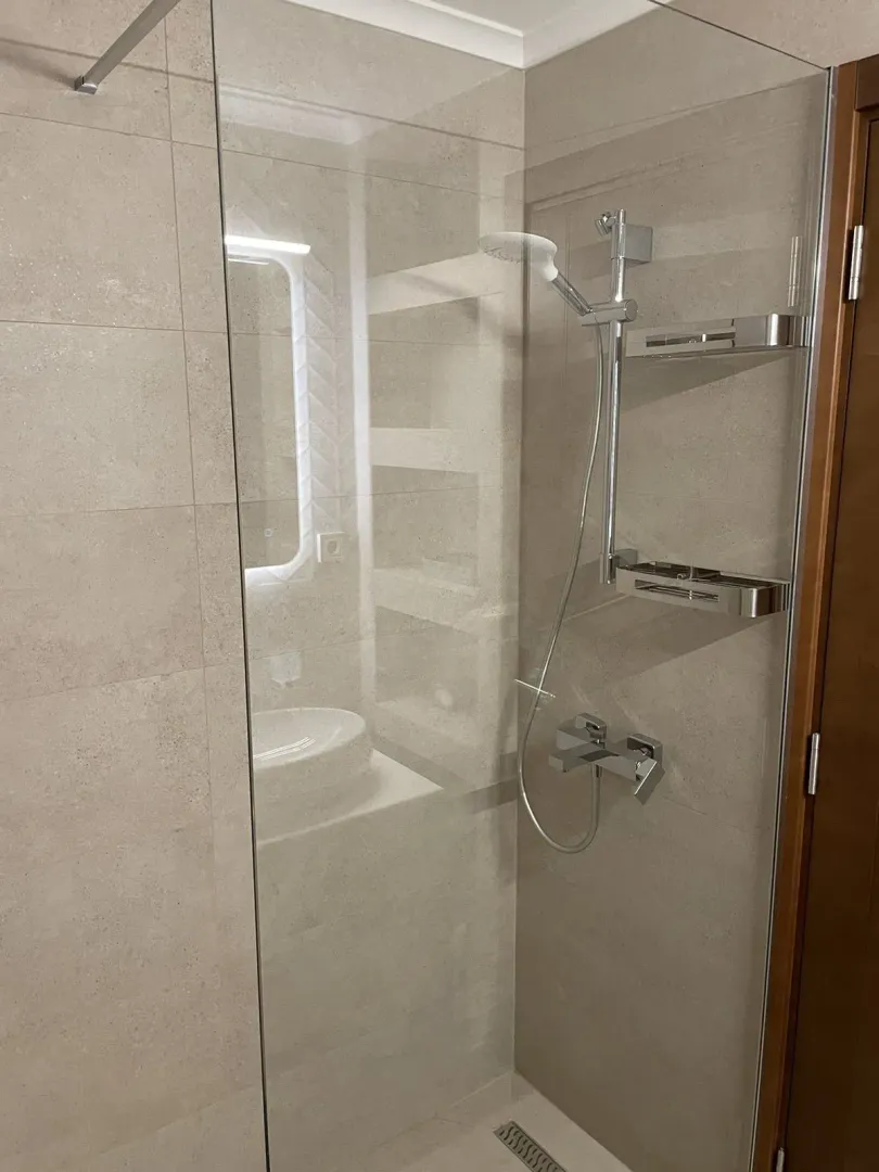 Modern shower with a glass cabin and light-colored tiles.
