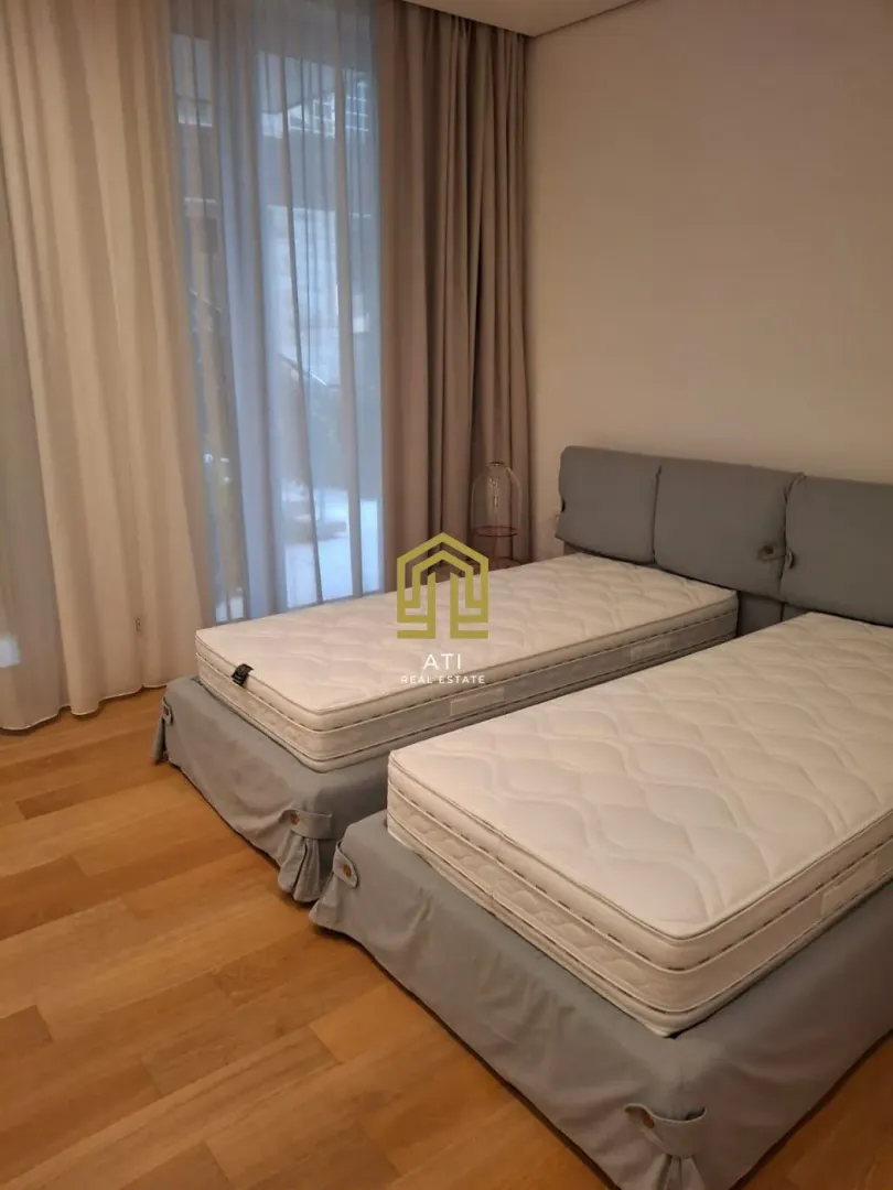 Spavaća soba sa dva odvojena kreveta i velikim prozorom sa zavjesama.