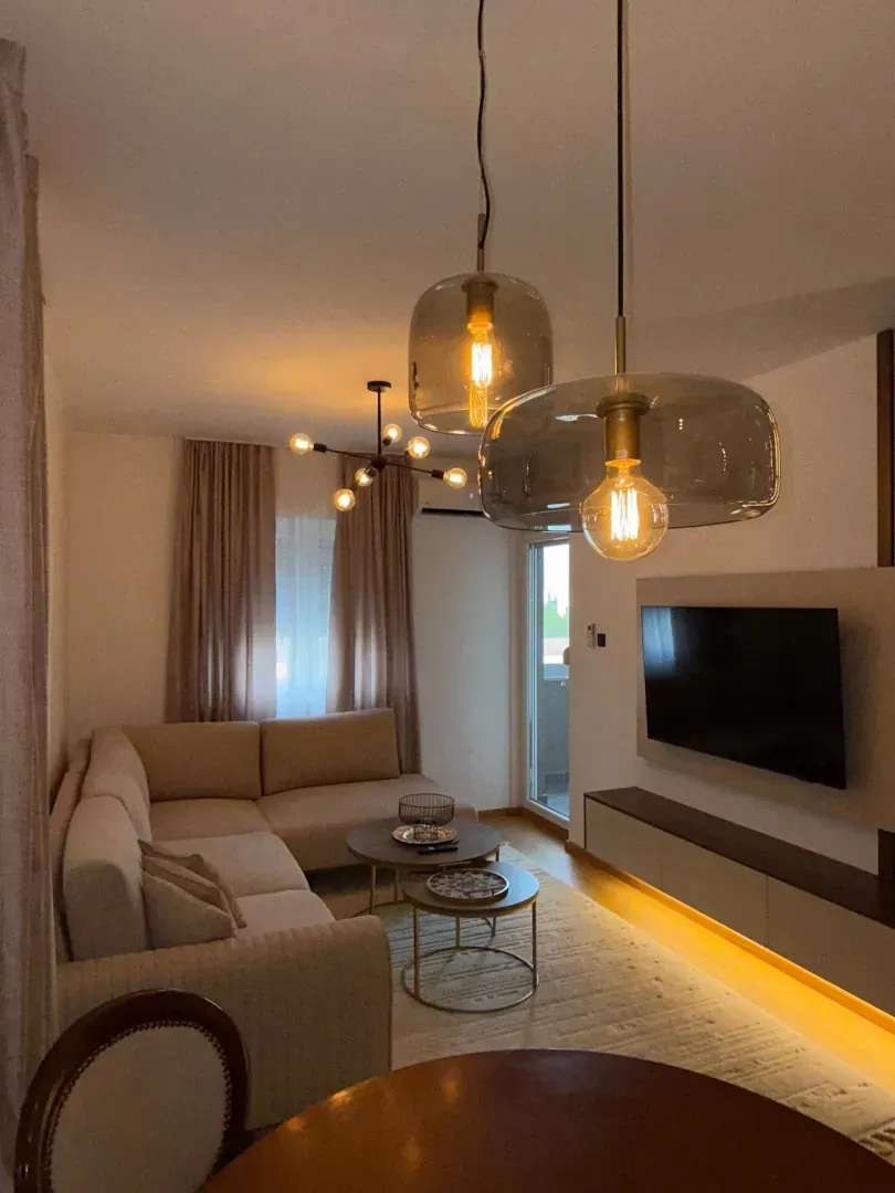 Udobna dnevna soba sa ugaonom garniturom, TV-om i modernim osvjetljenjem.