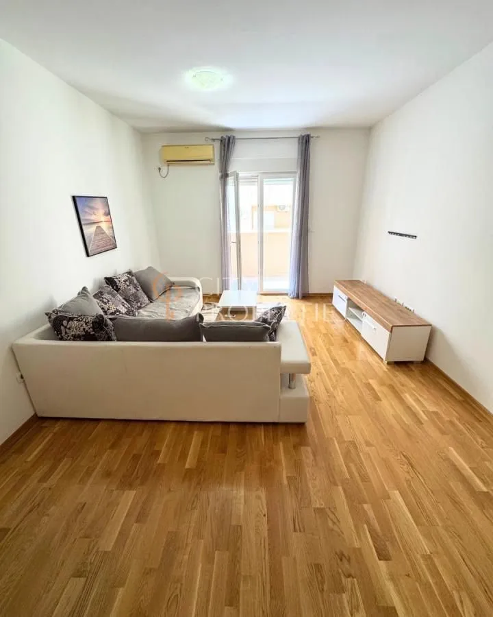 Dnevna soba sa garniturom, drvenim podom i izlazom na terasu.