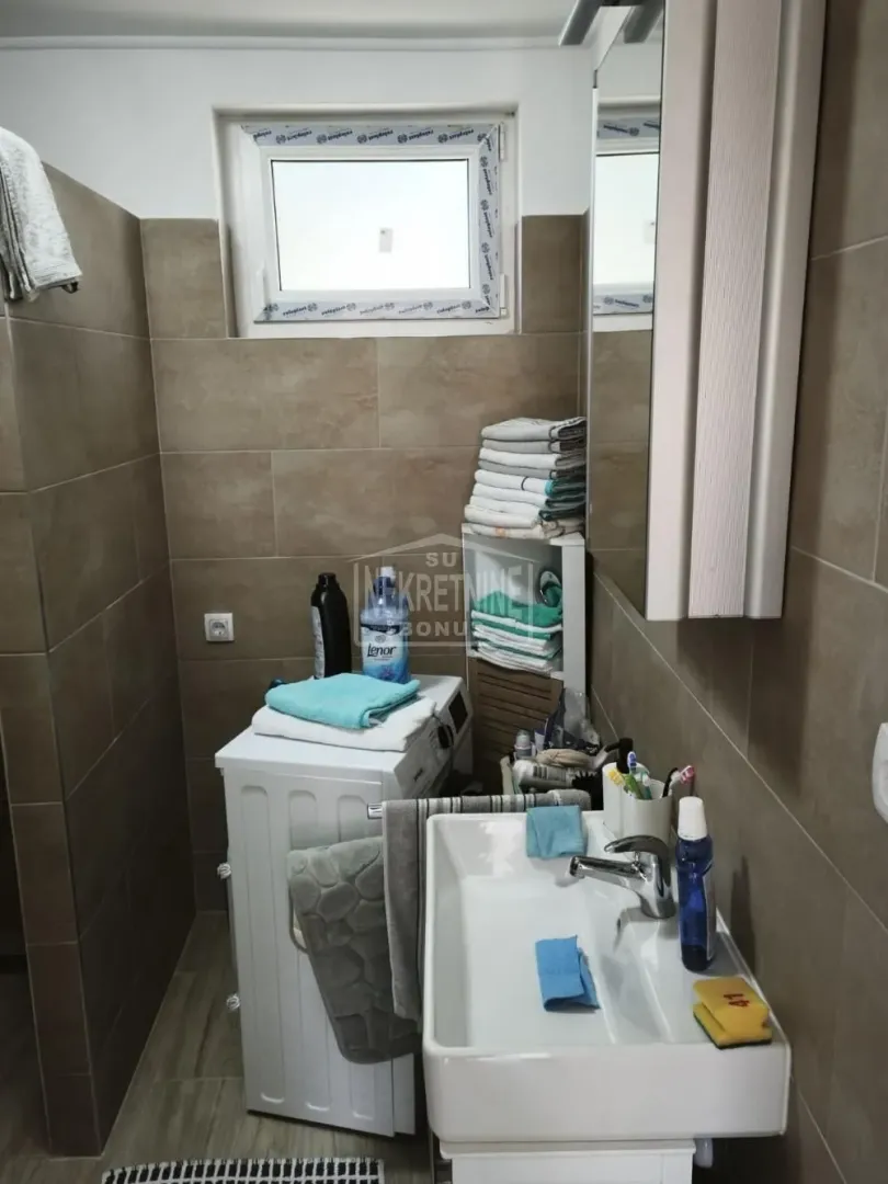 Manje kupatilo sa umivaonikom, veš mašinom i pločicama braon boje.