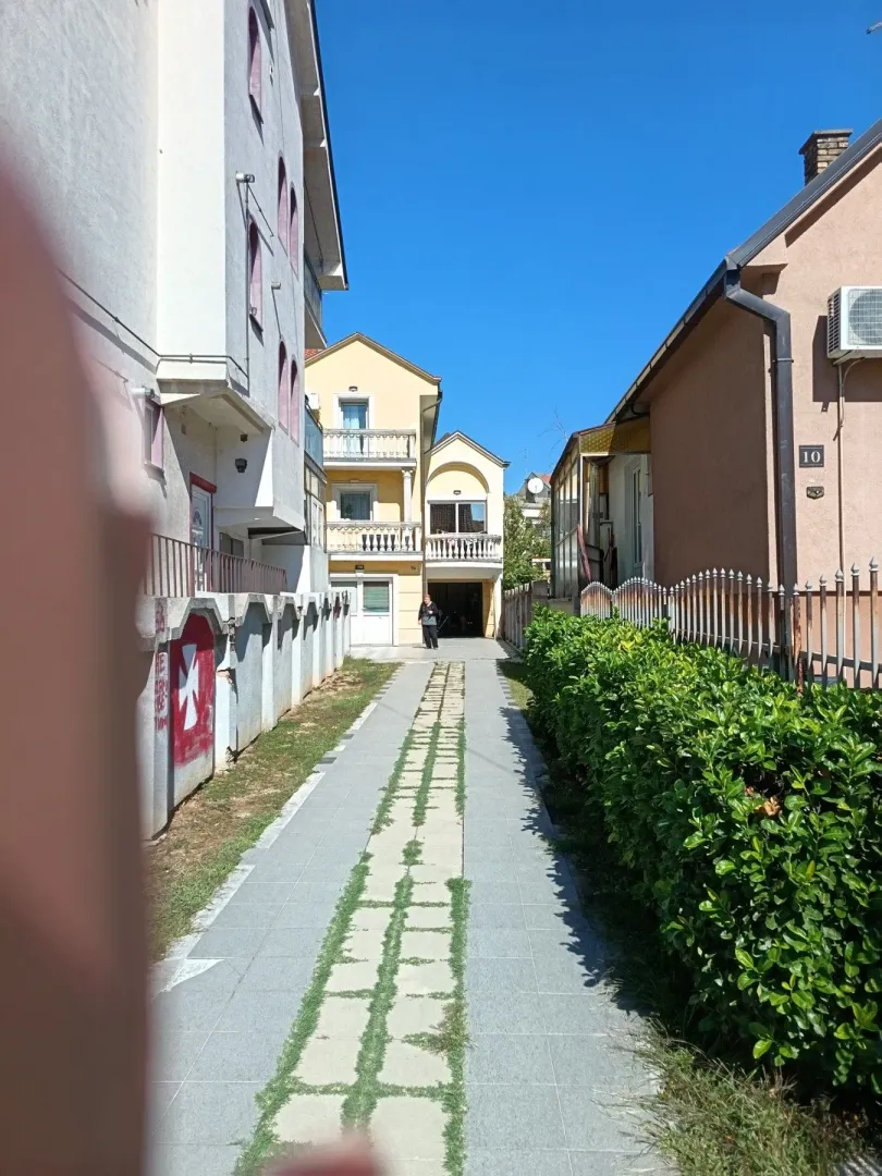 Pogled na popločanu stazu između stambenih objekata.