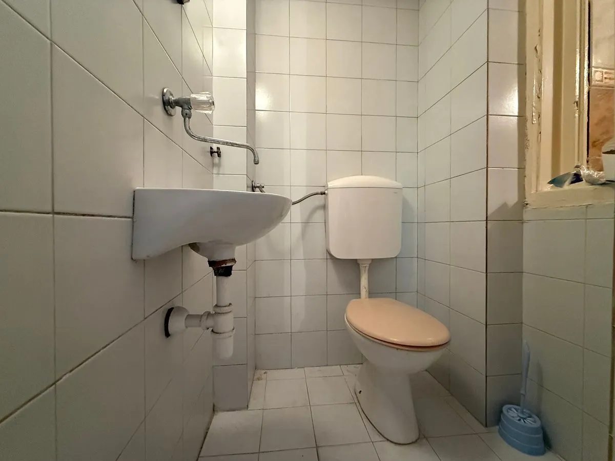 Manje kupatilo obloženo belim pločicama sa umivaonikom i wc šoljom.