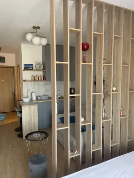 Living room with a wooden partition shelving unit and a kitchen in the background. - image 2