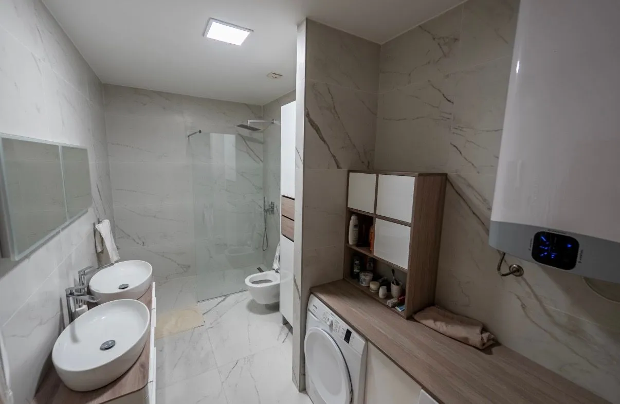 Modern bathroom with two sinks, a walk-in shower, and a washing machine.