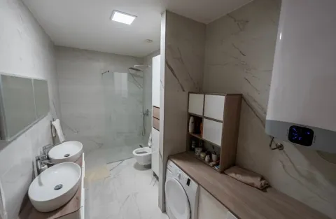 Modern bathroom with two sinks, a walk-in shower, and a washing machine. - image 8