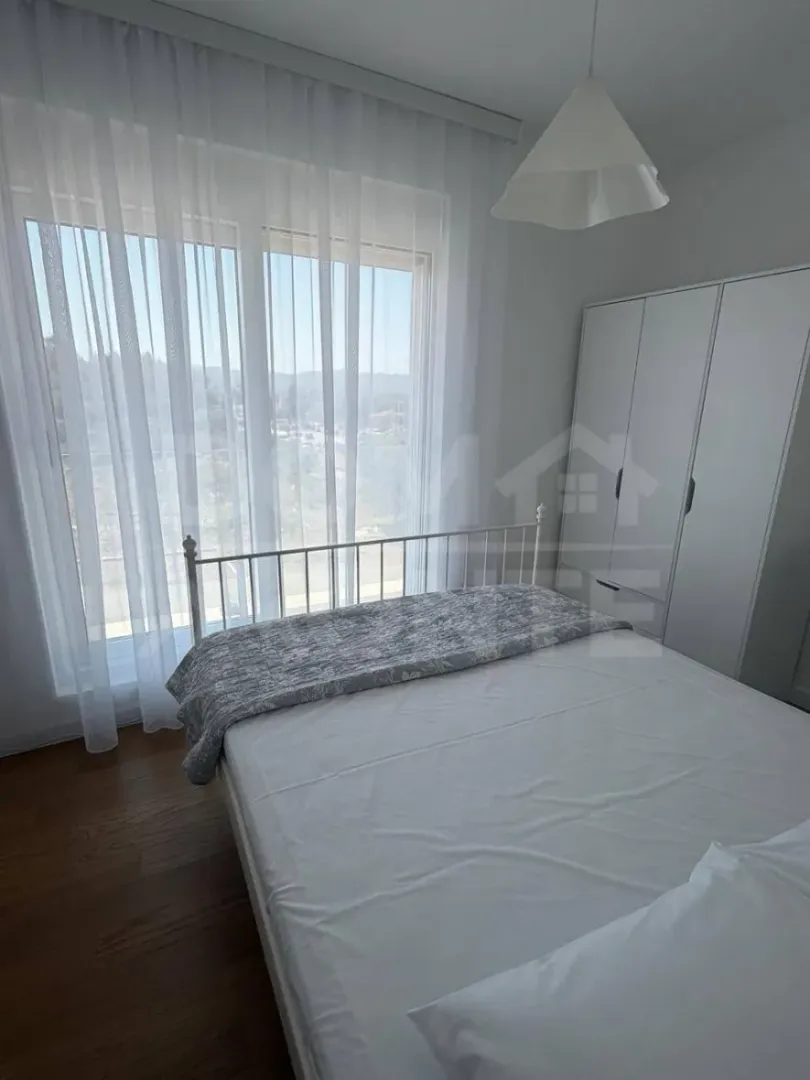 Svjetla spavaća soba sa bračnim krevetom, bijelim garderoberom i velikim prozorom.