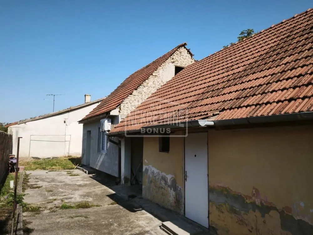 Pogled na dvorište i spoljašnjost starije kuće sa krovom od crepa.