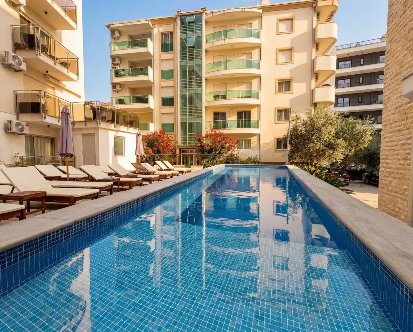 View of the outdoor swimming pool with sun loungers and a building in the background.